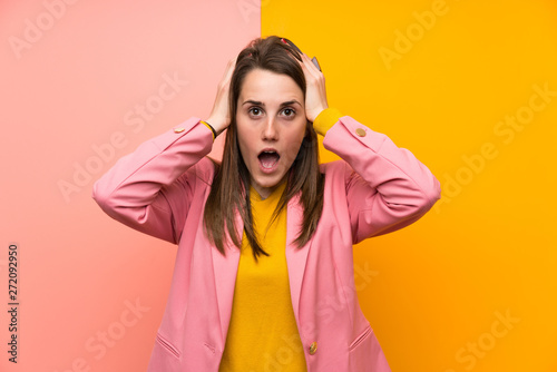 Young woman with pink suit over colorful background with surprise facial expression © luismolinero