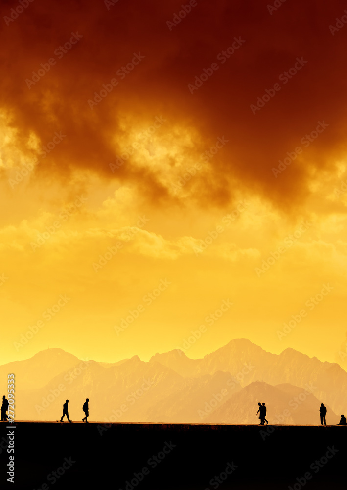 Silhouetted people over mountains and sunset sky