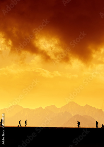 Silhouetted people over mountains and sunset sky