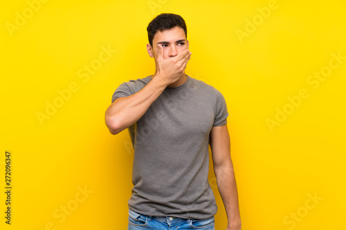 Handsome man over isolated yellow wall covering mouth with hands