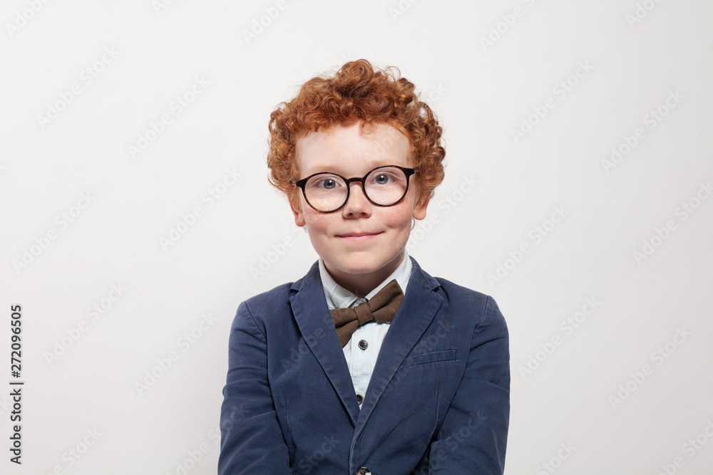 Cute child in glasses and blue suit portrait. Funny redhead boy on white background