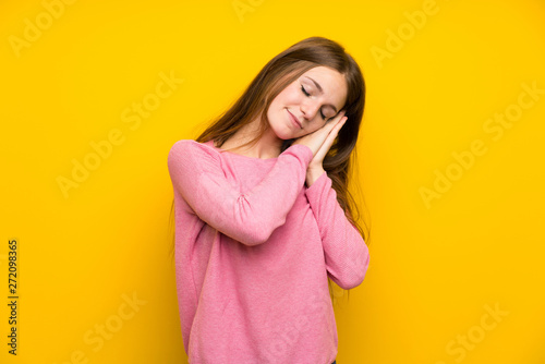 Young woman with long hair over isolated yellow wall making sleep gesture in dorable expression