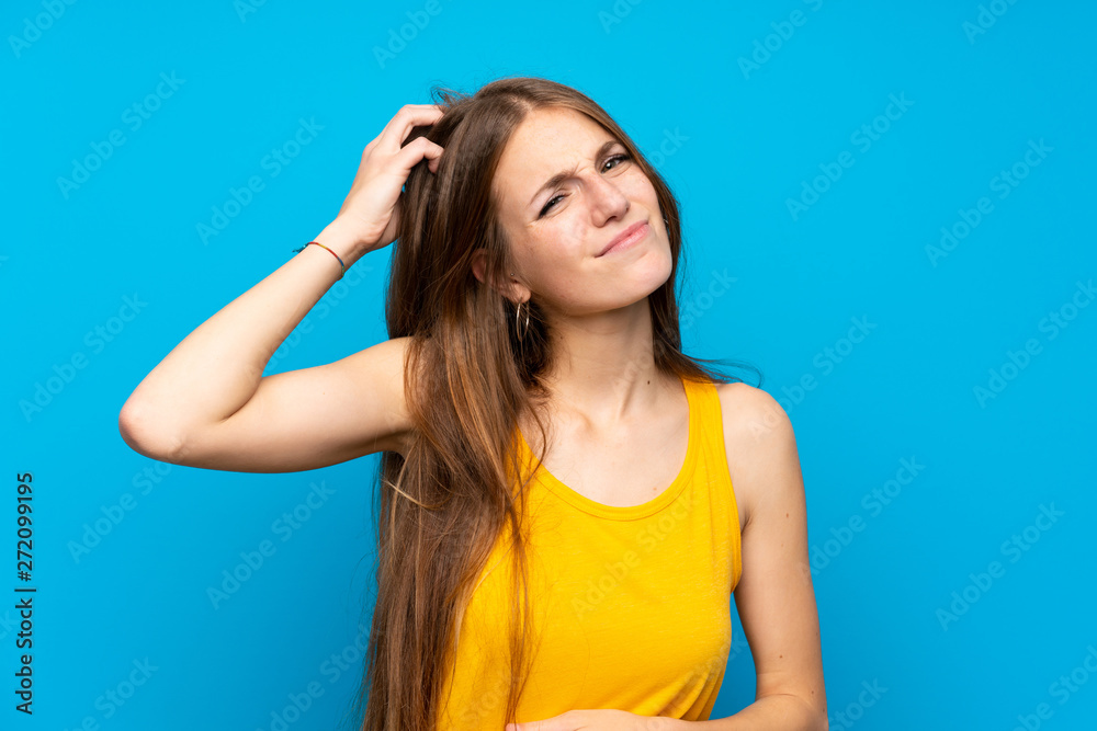 Young woman with long hair over isolated blue wall having doubts while scratching head