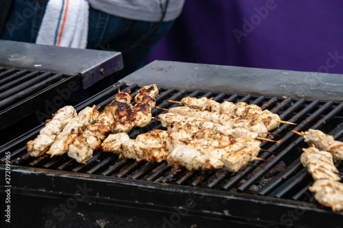 Large open outdoor barbecue grill cooking kabob made of chunks of chicken on wooden skewers.
