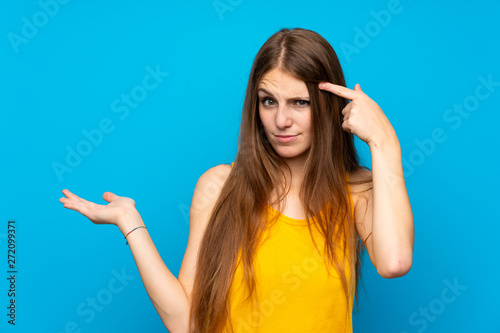 Young woman with long hair over isolated blue wall making the gesture of madness putting finger on the head