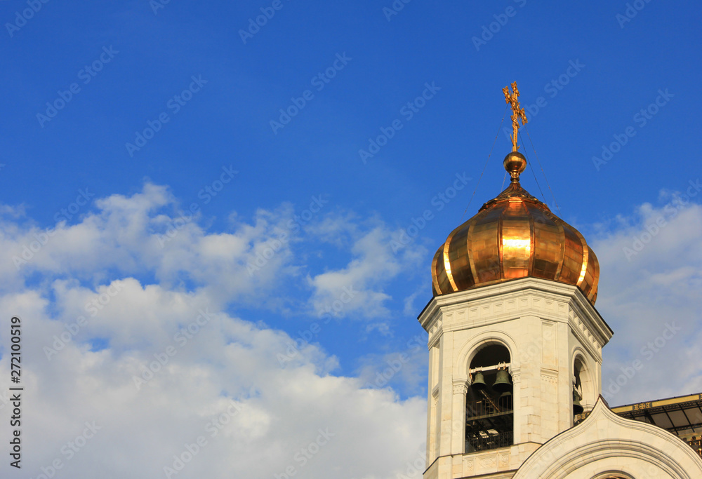 Church golden dome and bell tower with cross on blue sky background 