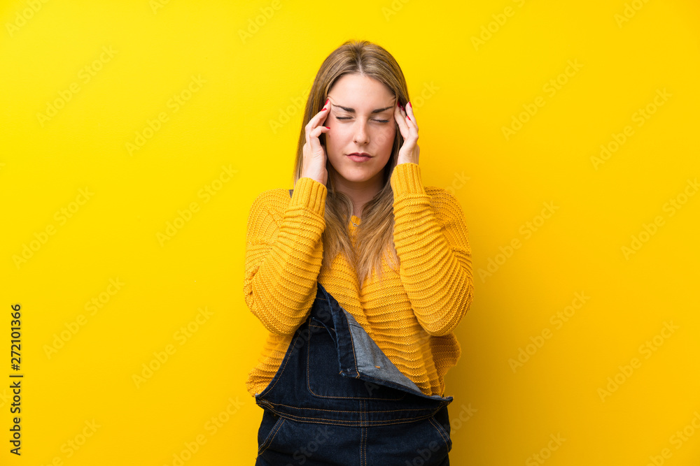 Woman with overalls over isolated yellow wall unhappy and frustrated with something. Negative facial expression Woman with overalls over isolated yellow wall unhappy and frustrated with something. Negative facial expression