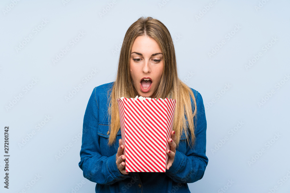 Obraz premium Blonde woman with popcorns over blue wall doing surprise gesture