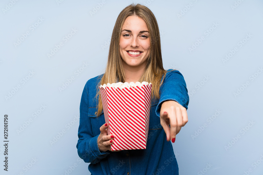 Obraz premium Blonde woman with popcorns over blue wall