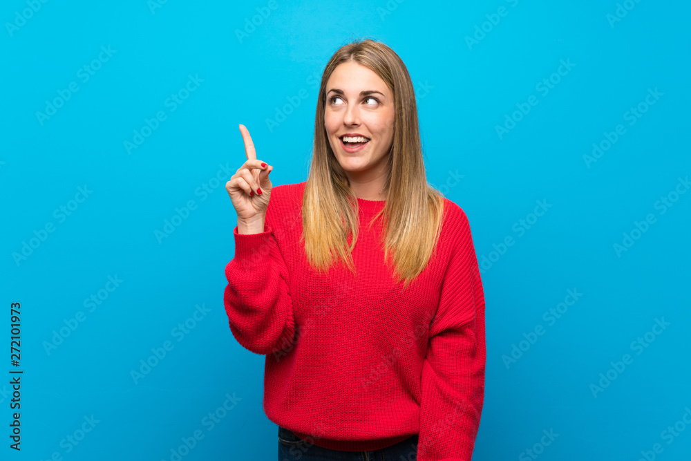 Woman with red sweater over blue wall intending to realizes the solution while lifting a finger up Woman with red sweater over blue wall intending to realizes the solution while lifting a finger up