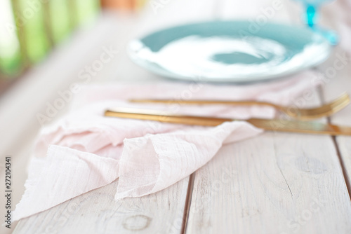 Table for guests, decorated with candles, served with cutlery and crockery and covered with a tablecloth blue plate and golden fork and knife on pink gauze napkin.