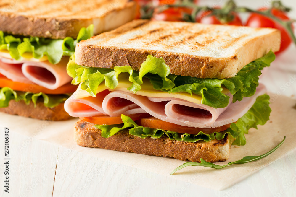 Close-up photo of a club sandwich. Sandwich with meat, prosciutto, salami, salad, vegetables, lettuce, tomato, onion and mustard on a fresh sliced rye bread on wooden background. Olives background. Close-up photo of a club sandwich. Sandwich with meat, prosciutto, salami, salad, vegetables, lettuce, tomato, onion and mustard on a fresh sliced rye bread on wooden background. Olives background.