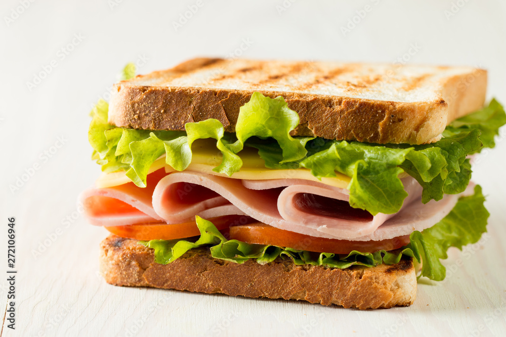 Close-up photo of a club sandwich. Sandwich with meat, prosciutto, salami, salad, vegetables, lettuce, tomato, onion and mustard on a fresh sliced rye bread on wooden background. Olives background. Close-up photo of a club sandwich. Sandwich with meat, prosciutto, salami, salad, vegetables, lettuce, tomato, onion and mustard on a fresh sliced rye bread on wooden background. Olives background.