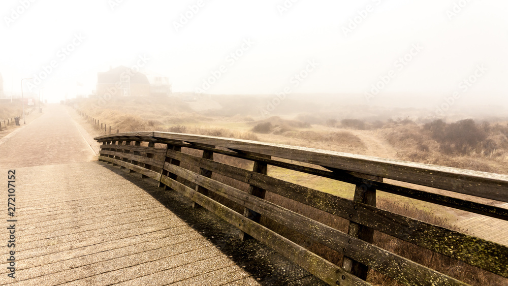 Fototapeta premium Wooden bridge and road. Autumnal misty morning on the coast of Texel island, the Netherlands.