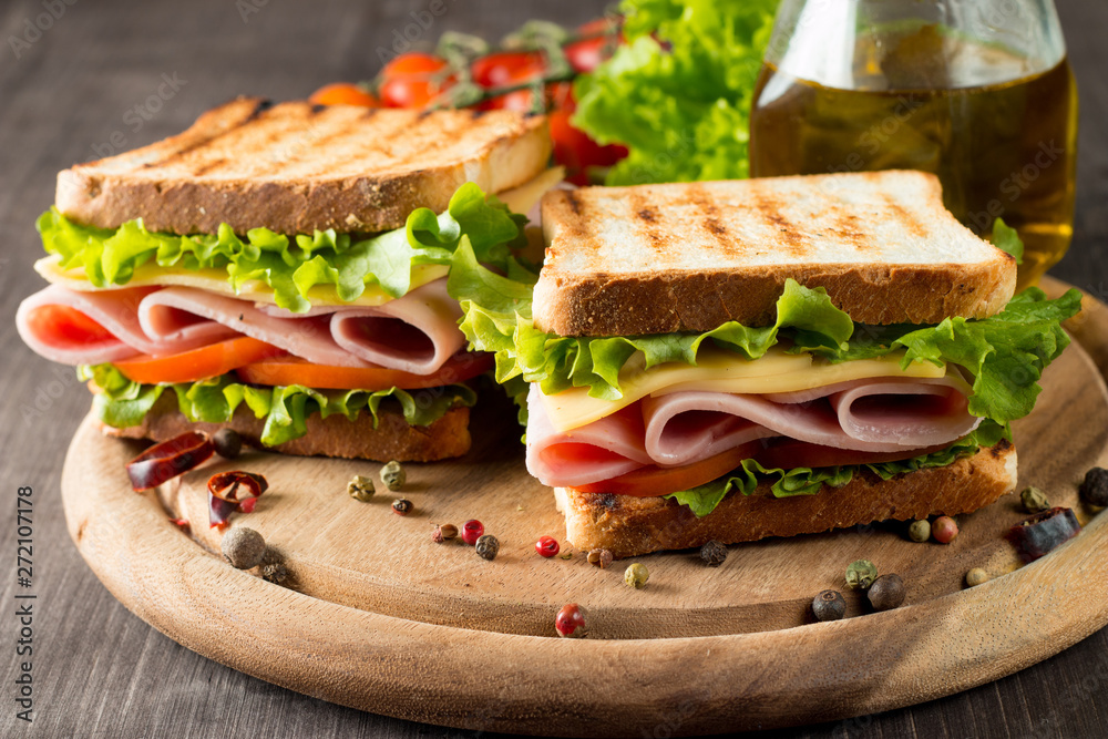 Close-up photo of a club sandwich. Sandwich with meat, prosciutto, salami, salad, vegetables, lettuce, tomato, onion and mustard on a fresh sliced rye bread on wooden background. Olives background. Close-up photo of a club sandwich. Sandwich with meat, prosciutto, salami, salad, vegetables, lettuce, tomato, onion and mustard on a fresh sliced rye bread on wooden background. Olives background.