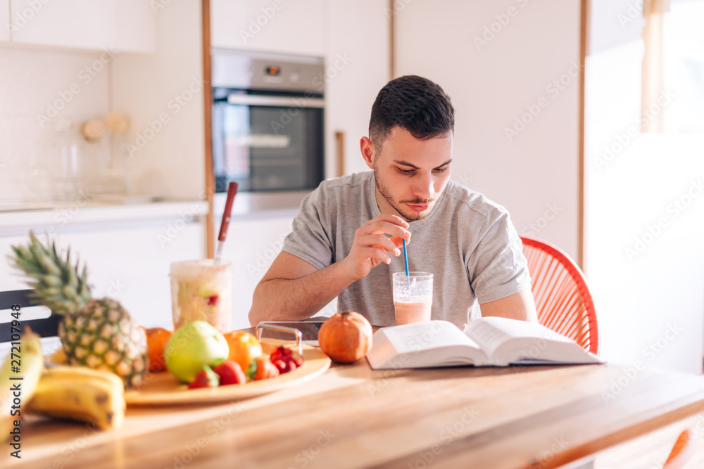 healthy strong young man reading a book early in the morning while making his smoothie.