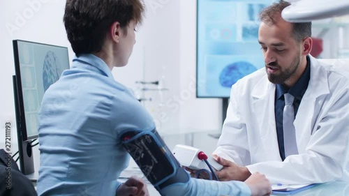 Caucasian physician measuring blood presure with a digital sphygmomanometer. Modern research facility with 3D brain simulation and DNA strings scans photo