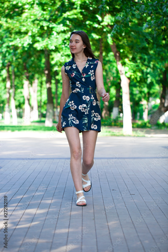 Young beautiful woman in a blue short dress walking on the road