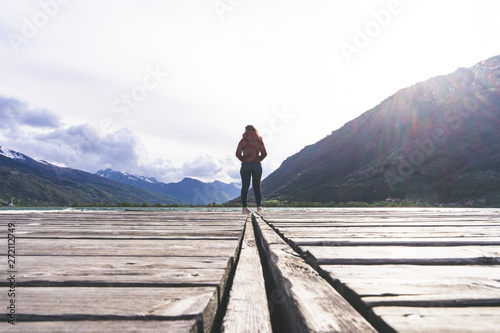 A young girl standing alone in the center of the frame looking out towards the seat. Peaceful and beautiful landscape. A long jetty  pier center of the image