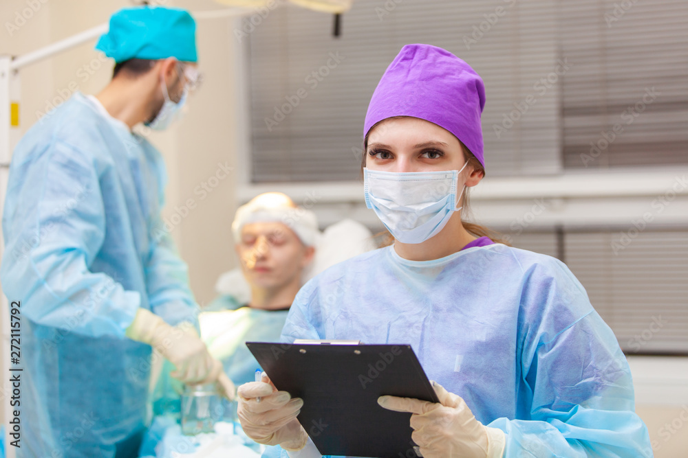 Beautiful portrait of a doctor with documents on the background of the operating room. Baldness treatment. Hair transplant. Surgeons in the operating room carry out hair transplant surgery. Surgical Beautiful portrait of a doctor with documents on the background of the operating room. Baldness treatment. Hair transplant. Surgeons in the operating room carry out hair transplant surgery. Surgical