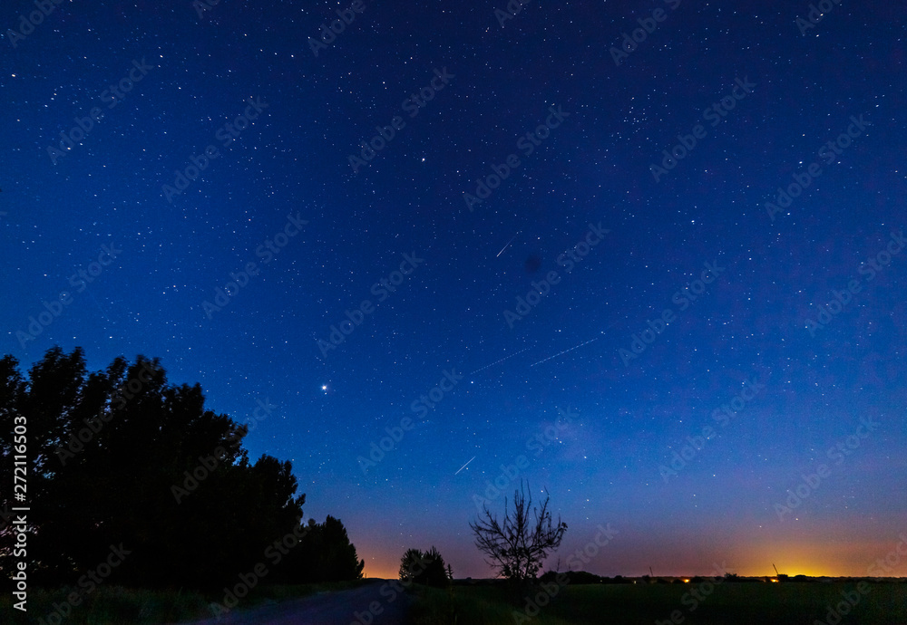 Starry sky after sunset over the field and trees. .