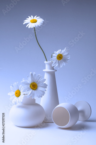 Blue still life with two vases, a wine glass and chamomile flowers.
