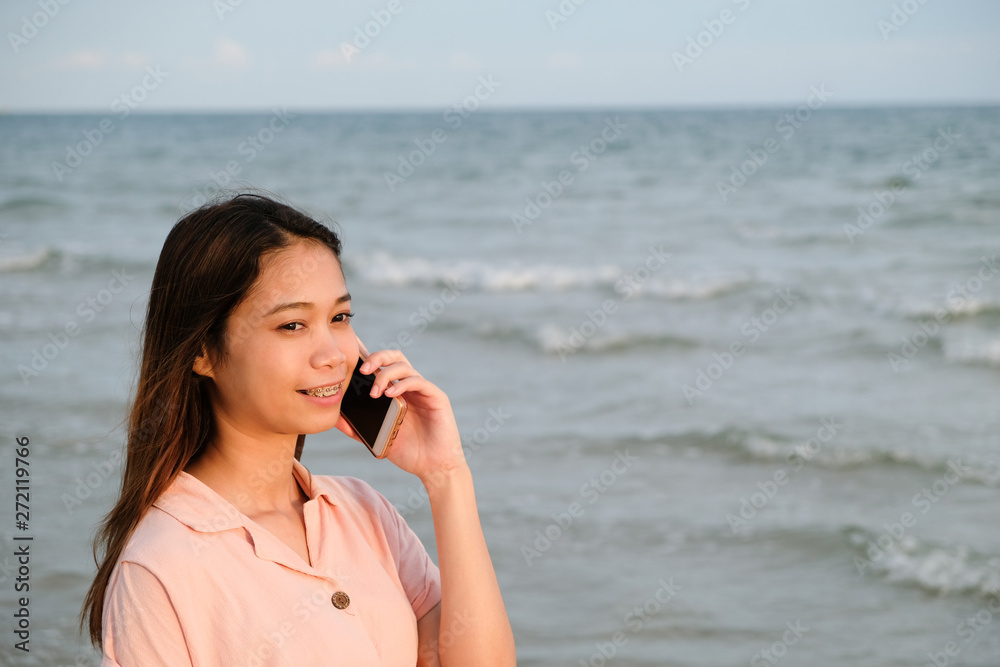 Asian woman talking on mobile phone standing on the beach Asian woman talking on mobile phone standing on the beach