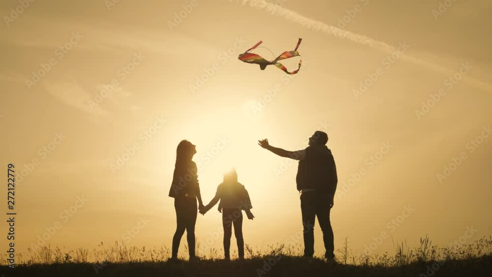 Happy family playing with a kite while on meadow, sunset, in summer day. Funny family time. Happy little girl launch a kite with parents. Mom, Dad and daughter are happy together. Happy family playing with a kite while on meadow, sunset, in summer day. Funny family time. Happy little girl launch a kite with parents. Mom, Dad and daughter are happy together.