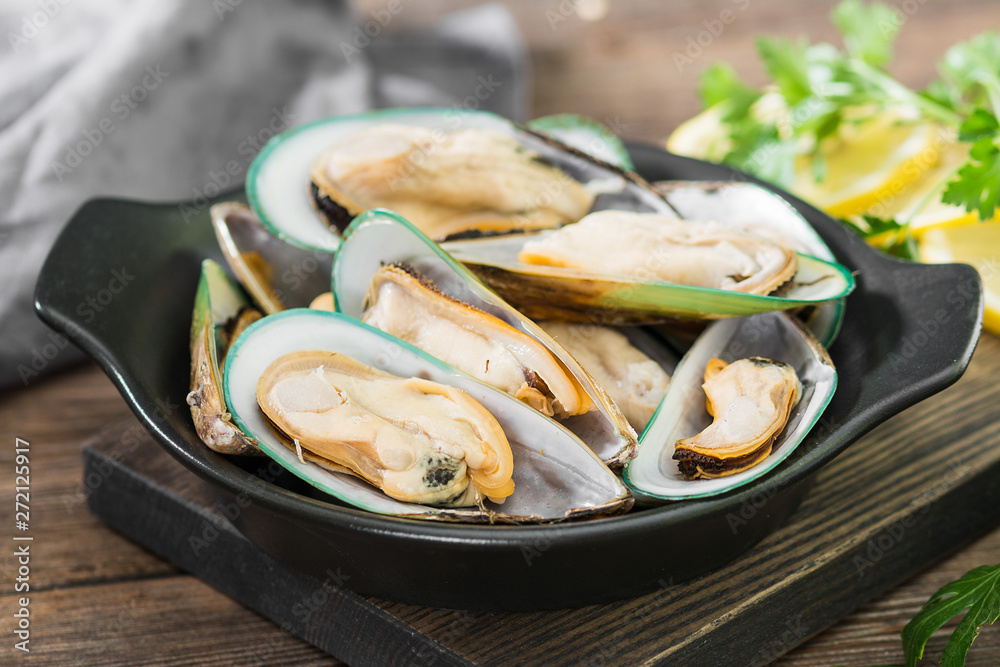 Raw kiwi mussels in a black plate on a wooden Board Raw kiwi mussels in a black plate on a wooden Board