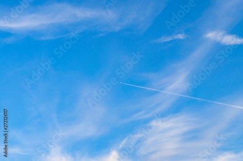 Blue sky with white clouds. White trail of an airplane on a background of bright blue sky.