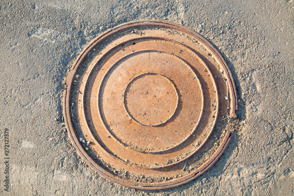 Manhole cast iron heavy brown with a pattern of several rings on the background of concrete screed.