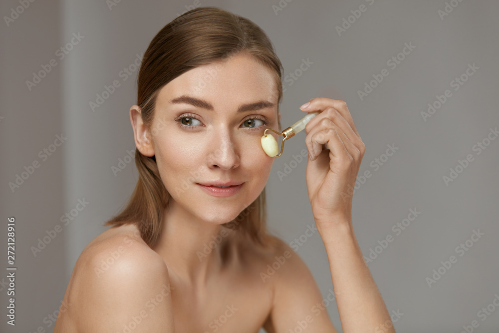 Woman using jade facial roller for face massage at home