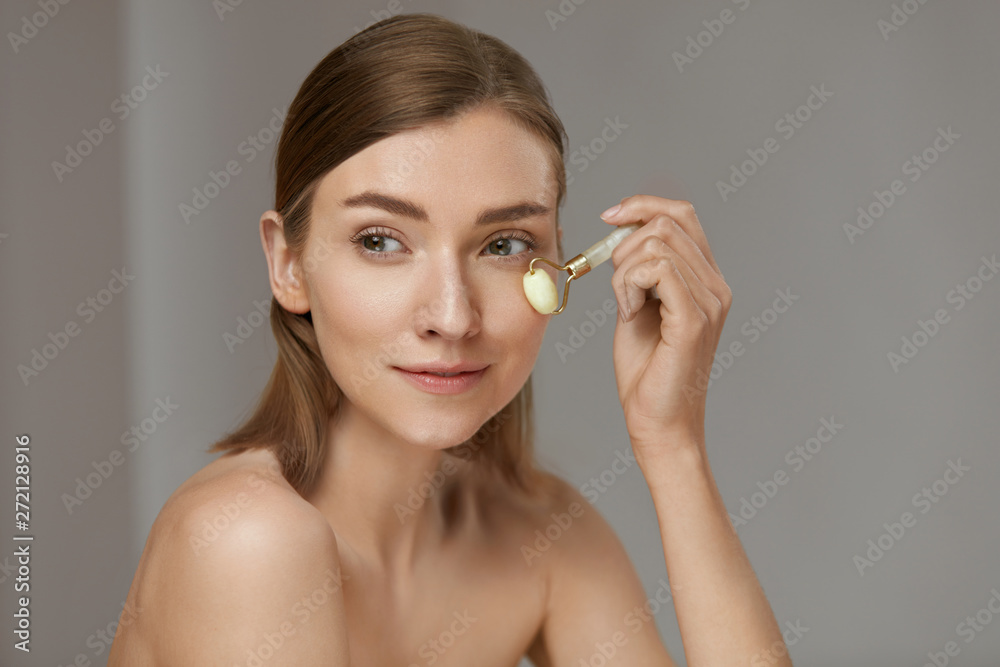 Woman using jade facial roller for face massage at home Woman using jade facial roller for face massage at home