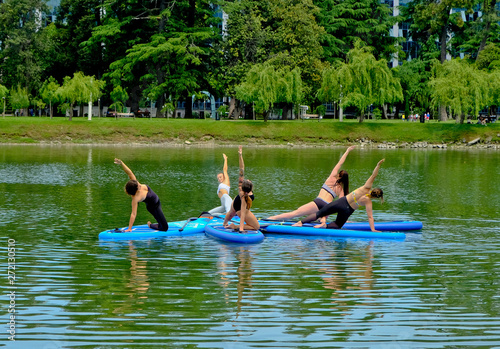 Yoga on sup board. Young girls paddling on SUP board on the lake at city. Group women is practicing (doing) yoga, fitness, pilates and meditation on a SUP board. Awesome active training in outdoor.  © Khrystyna Bohush