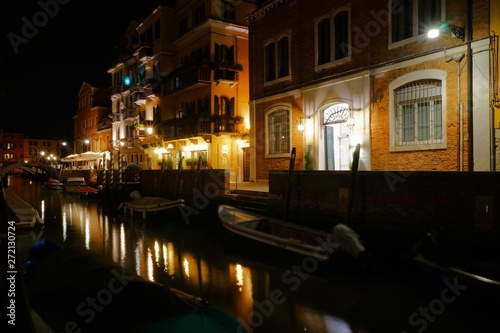 Night view of a quiet venetian canal with moored boats and street lights