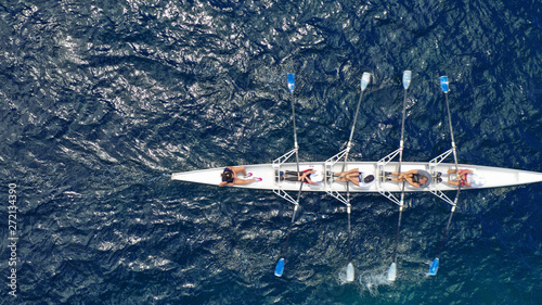 Aerial drone bird's eye view of sport canoe operated by team of young trained athletes in deep blue Aegean sea