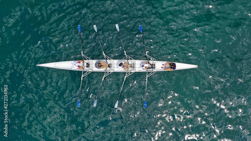 Aerial drone bird's eye view of sport canoe operated by team of young trained athletes in deep blue Aegean sea