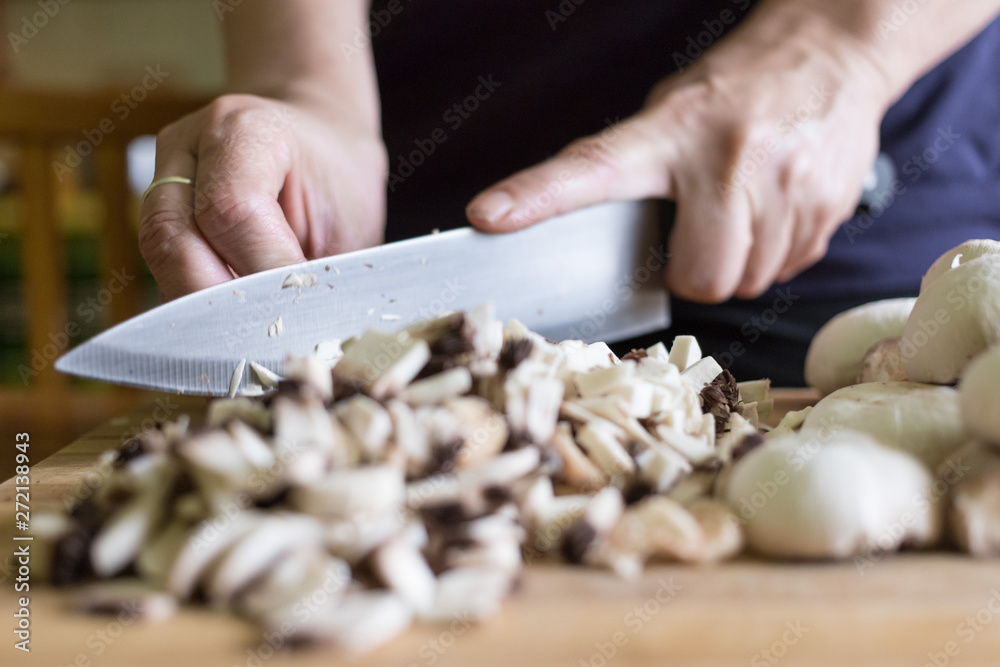 A woman cuts mushrooms with a knife on a wooden cutting board