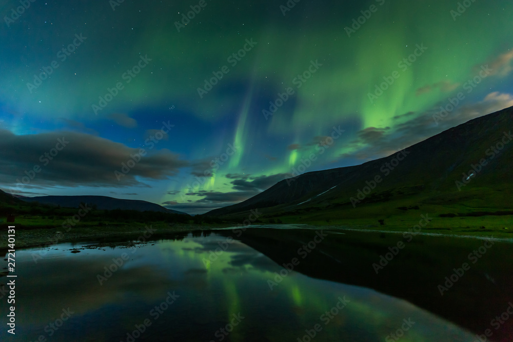 aurora borealis in the night sky cut the mountains, reflected in the water.