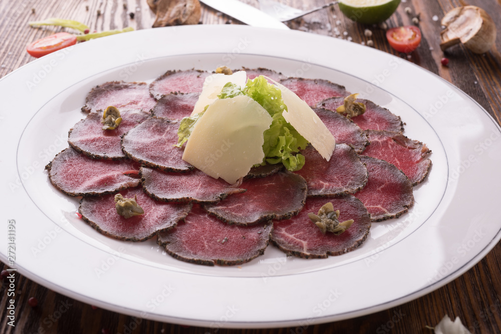 Marbled beef carpaccio decorated with greens and cheese on plate