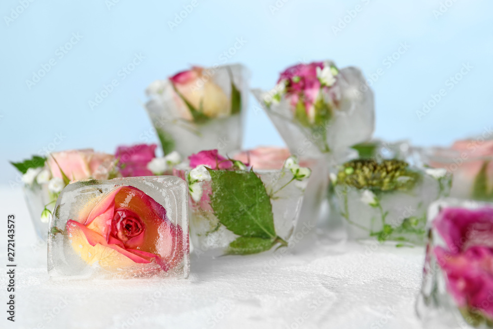 Ice cubes with flowers on table against color background Ice cubes with flowers on table against color background
