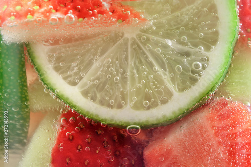 Refreshing fruit sparkling water from strawberries and lime in a glass mug close-up, background.
