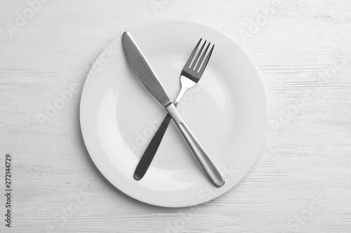 Empty plate with cutlery on white wooden background, flat lay