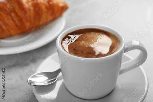 Cup of fresh coffee and croissant on grey table. Space for text