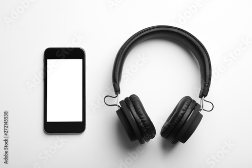 Stylish headphones and modern phone on white background, top view. Space for text