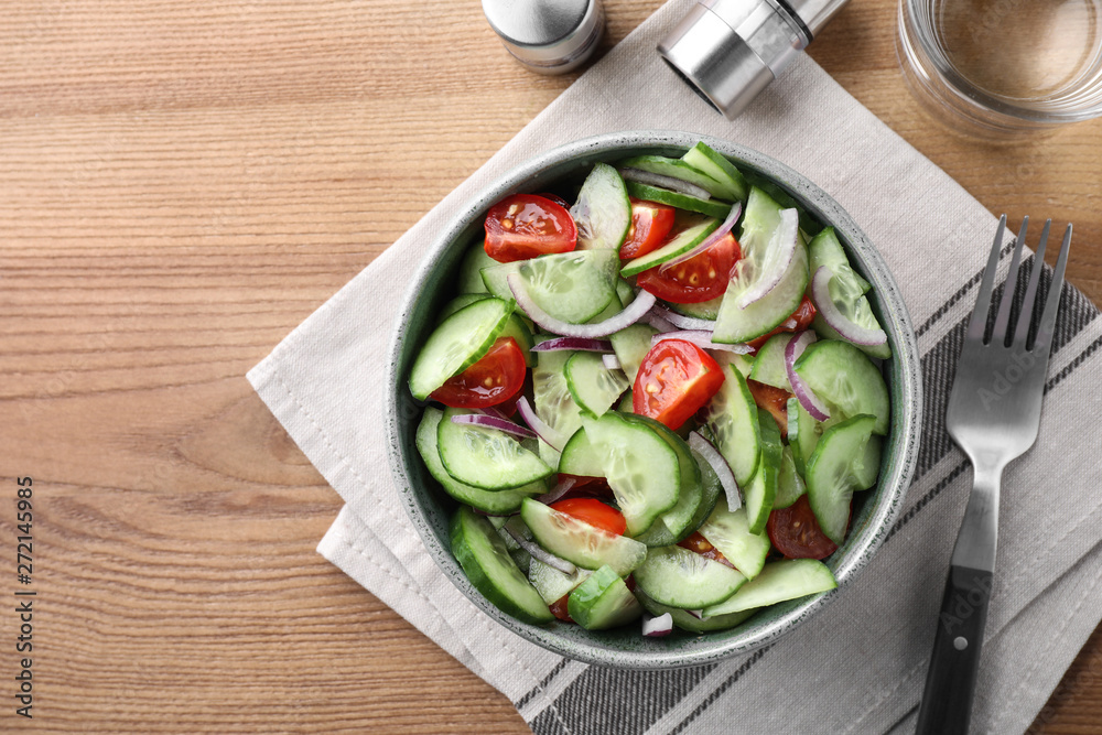 Bowl of tasty cucumber tomato salad served on wooden table, flat lay. Space for text Bowl of tasty cucumber tomato salad served on wooden table, flat lay. Space for text