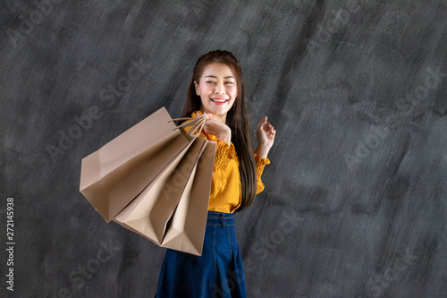 Shopping Woman, Beautiful Asian well-dressed young irl holding a brown blank paper bag and makes purchases in an online store against a black wall background with copy space for text or design. photo