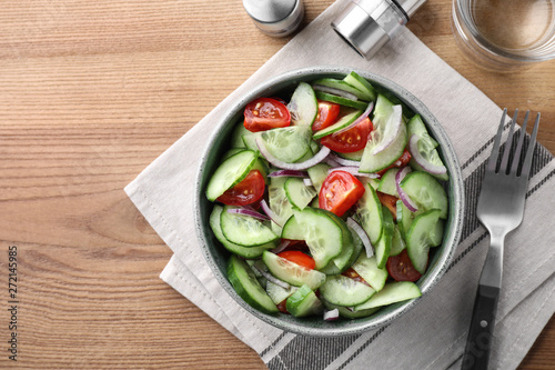 Bowl of tasty cucumber tomato salad served on wooden table, flat lay. Space for text
