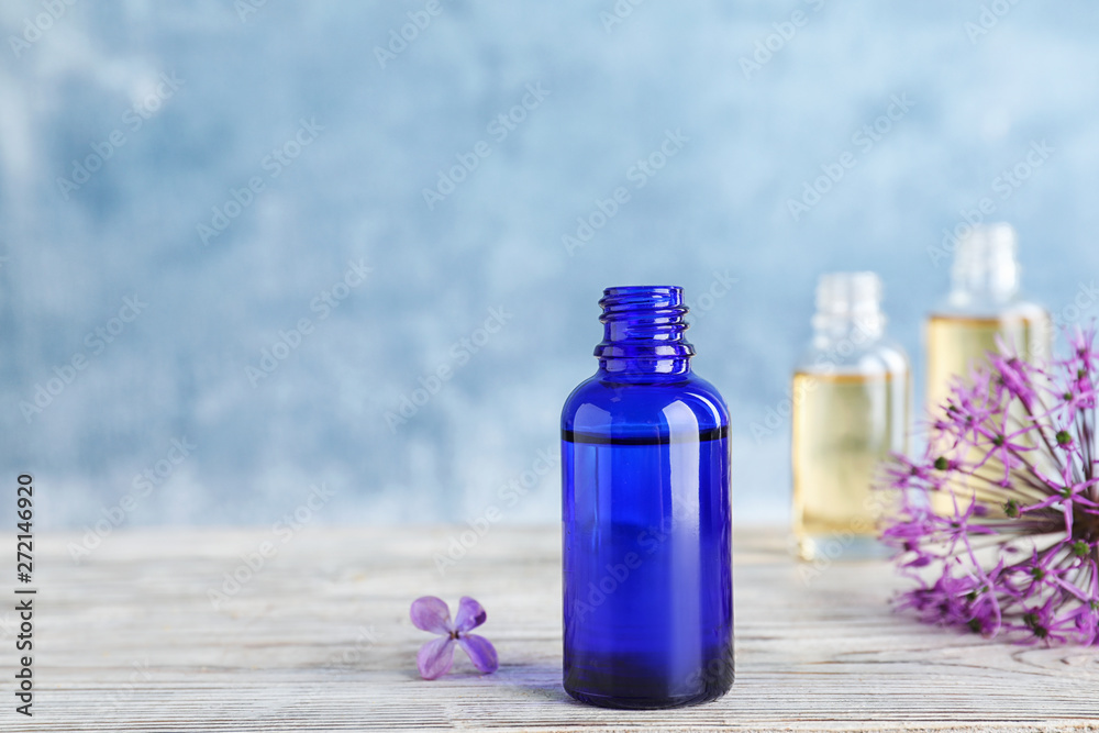 Bottle of essential oil with flowers on wooden table against color background, space for text