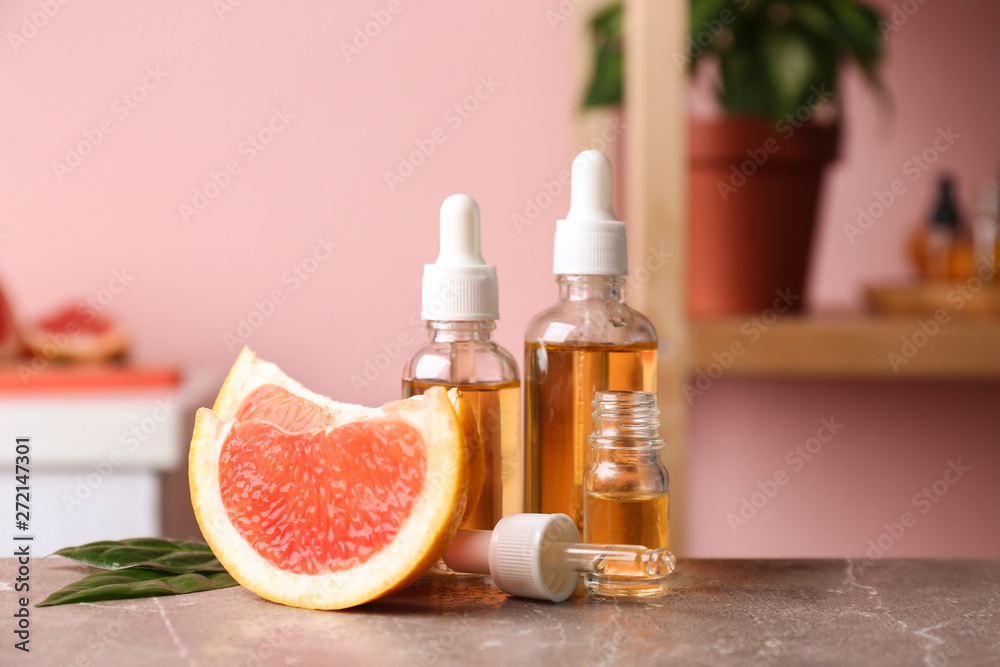 Bottles of essential oil and grapefruit slices on table against blurred background Bottles of essential oil and grapefruit slices on table against blurred background